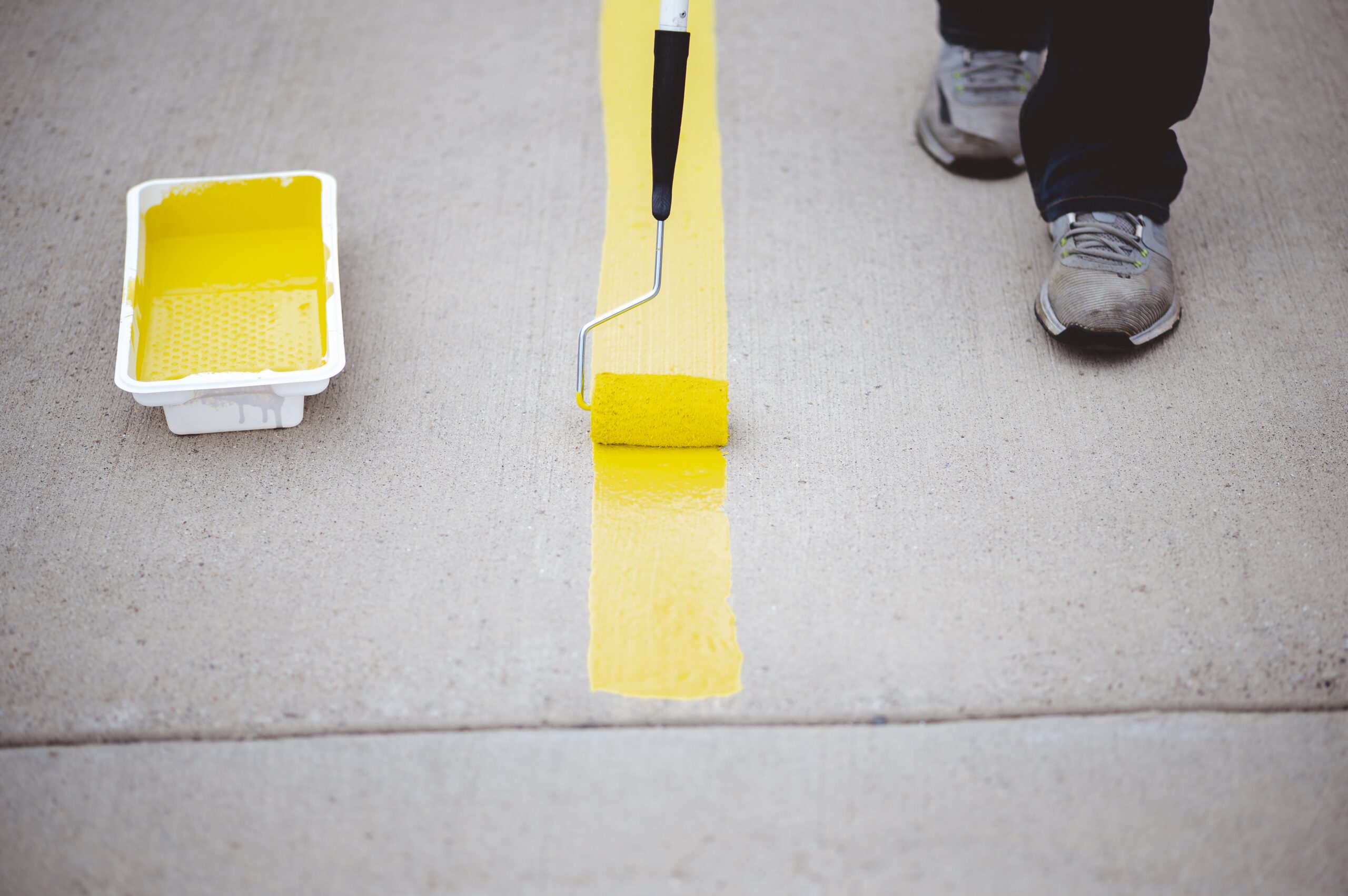 view of a person repainting the parking lines of the asphalt of a parking lot with yellow paint